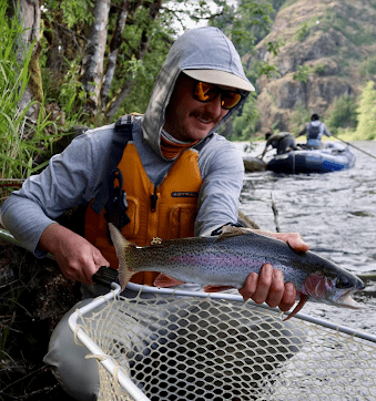 man holding net with fish next to river